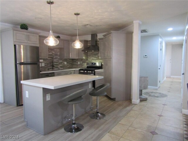 kitchen featuring a breakfast bar, stainless steel appliances, sink, wall chimney range hood, and hanging light fixtures