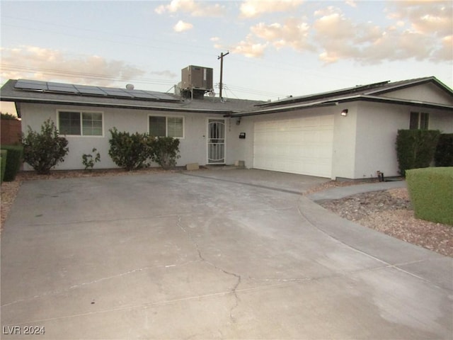 single story home featuring cooling unit, a garage, and solar panels