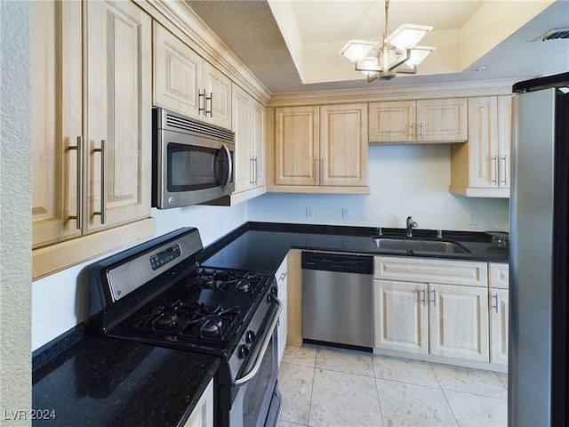 kitchen with a tray ceiling, stainless steel appliances, a chandelier, and sink