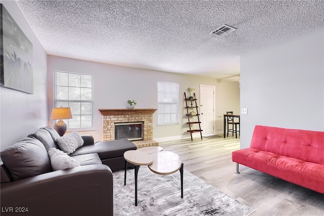 living room featuring a fireplace, a textured ceiling, plenty of natural light, and light hardwood / wood-style floors