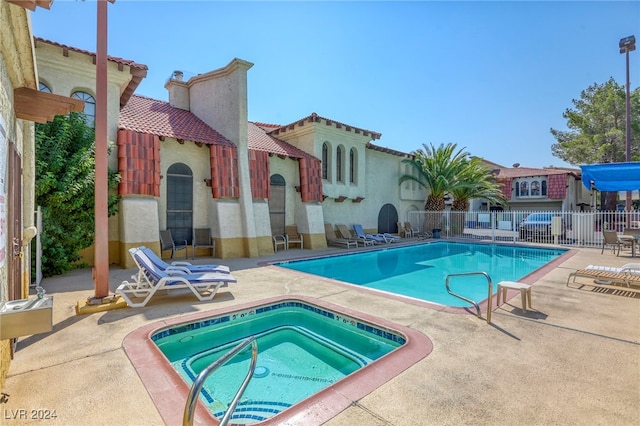 pool with a patio area, fence, and a hot tub