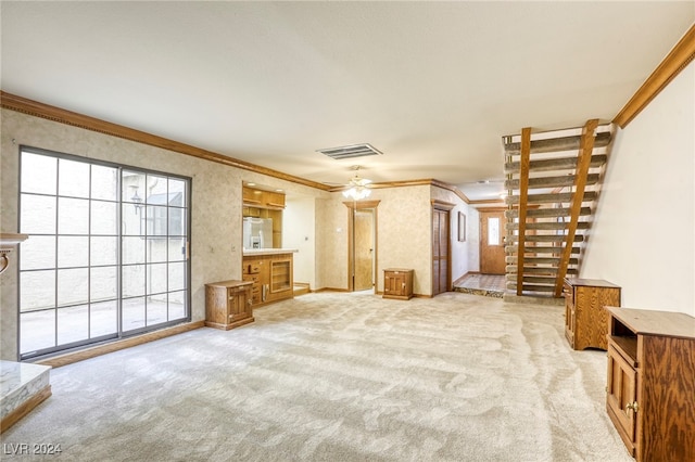 unfurnished living room with visible vents, baseboards, light colored carpet, ceiling fan, and ornamental molding