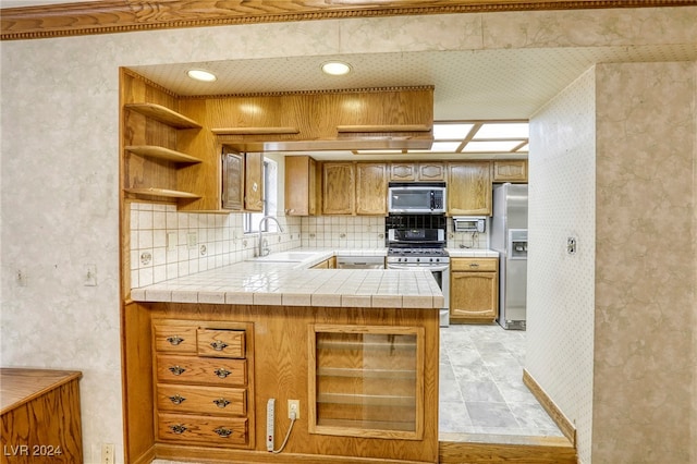 kitchen with stainless steel appliances, tile counters, brown cabinetry, and a sink