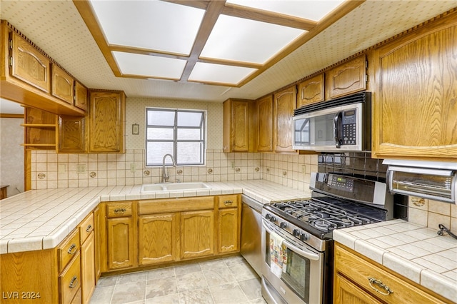 kitchen with tile countertops, appliances with stainless steel finishes, brown cabinetry, and a sink