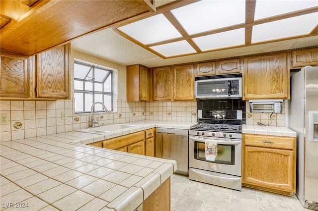 kitchen with tile countertops, tasteful backsplash, appliances with stainless steel finishes, and a sink