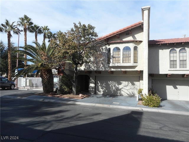 mediterranean / spanish-style house with a garage, concrete driveway, a tile roof, and stucco siding