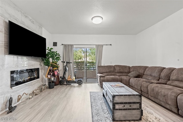 living room with light wood-type flooring, a high end fireplace, and a textured ceiling