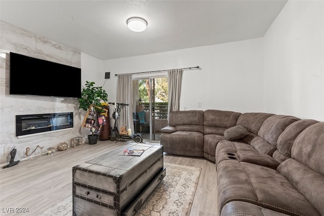 living room with a high end fireplace, light wood-type flooring, and a textured ceiling