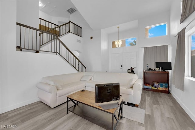 living room featuring a towering ceiling, a notable chandelier, and light hardwood / wood-style floors