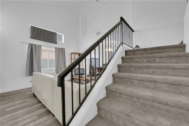 stairs with wood-type flooring and a towering ceiling