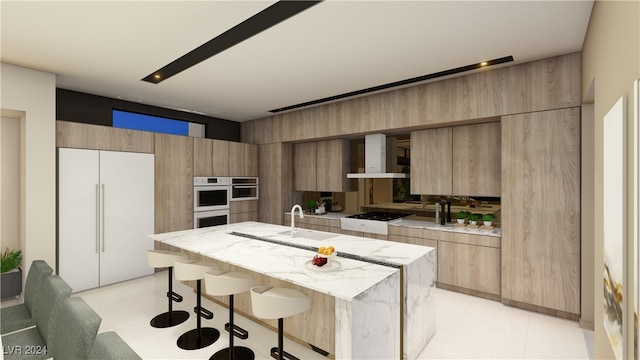 kitchen with white appliances, light stone countertops, wall chimney range hood, a breakfast bar area, and a kitchen island with sink