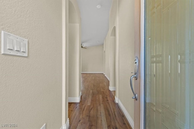 hall featuring arched walkways, dark wood-style flooring, a textured wall, and baseboards