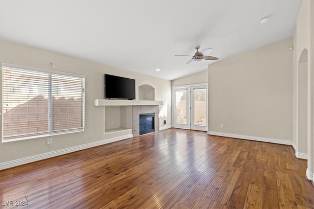 unfurnished living room with a tiled fireplace, wood finished floors, and a wealth of natural light