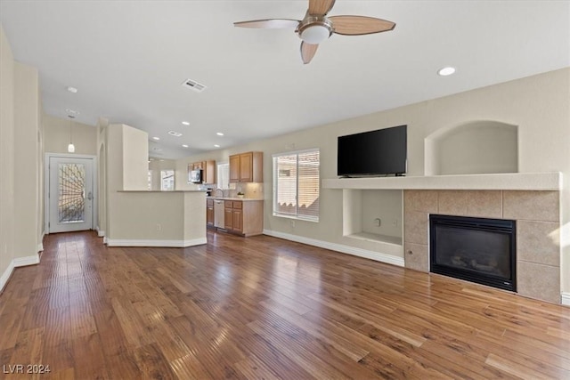 unfurnished living room with baseboards, visible vents, a ceiling fan, a tile fireplace, and dark wood-style flooring