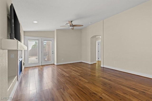 unfurnished living room featuring baseboards, arched walkways, a ceiling fan, a glass covered fireplace, and hardwood / wood-style floors