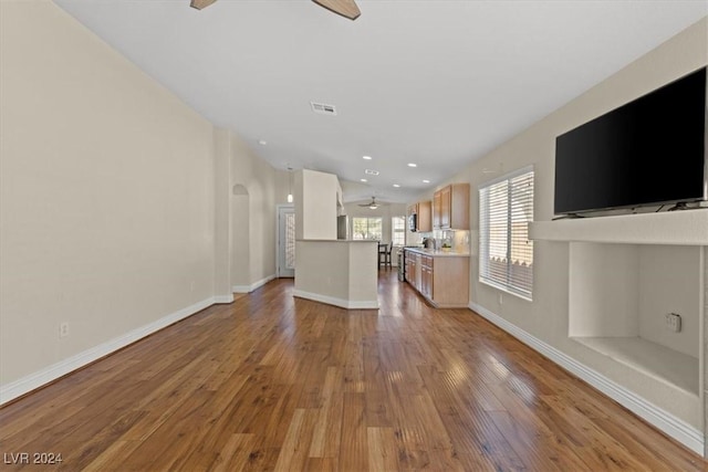 unfurnished living room with arched walkways, visible vents, ceiling fan, wood finished floors, and baseboards