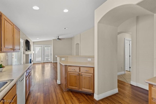 kitchen with arched walkways, light countertops, dishwashing machine, and hardwood / wood-style flooring