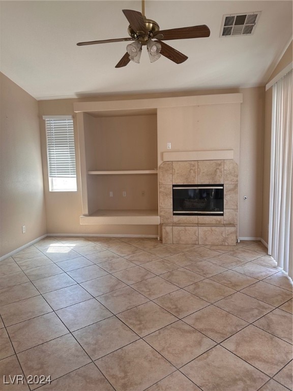 unfurnished living room with ceiling fan, a tiled fireplace, light tile patterned floors, and vaulted ceiling