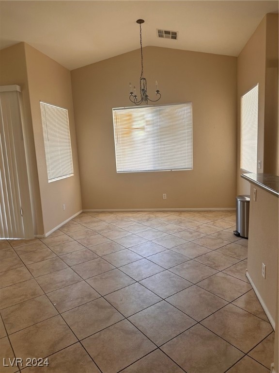 tiled empty room with lofted ceiling and an inviting chandelier