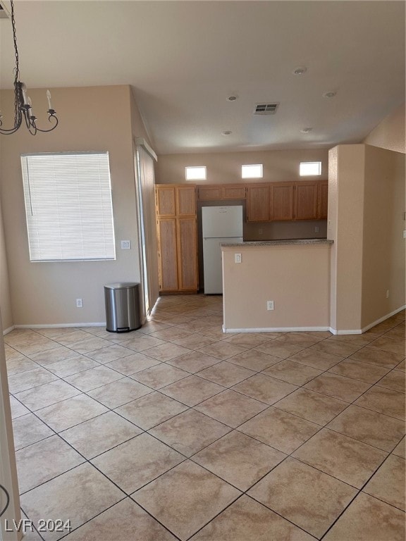 kitchen with white refrigerator, hanging light fixtures, light tile patterned floors, and a notable chandelier