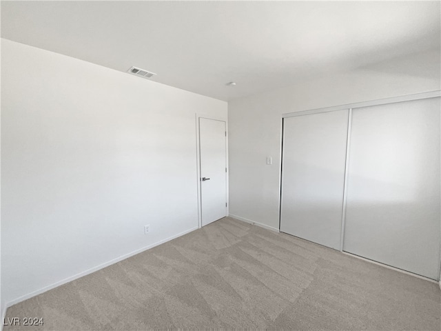 unfurnished bedroom with light colored carpet and a closet