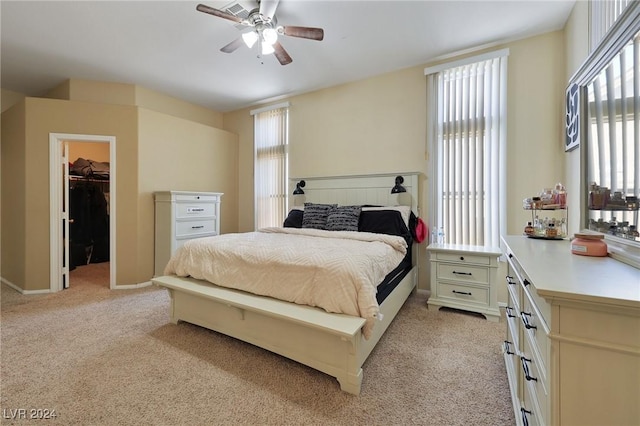 bedroom featuring baseboards, ceiling fan, light colored carpet, and a walk in closet