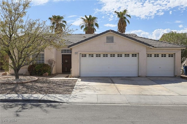 ranch-style house featuring concrete driveway, a tiled roof, an attached garage, and stucco siding