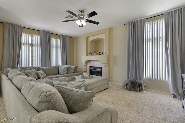 living room featuring a tiled fireplace, ceiling fan, and carpet