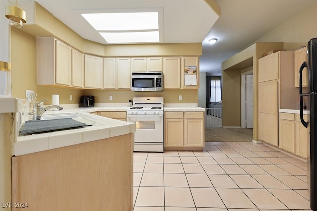 kitchen with light brown cabinetry, a sink, white gas range, tile countertops, and stainless steel microwave