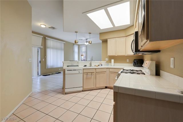 kitchen with white appliances, a skylight, light tile patterned floors, kitchen peninsula, and sink