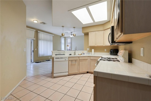 kitchen featuring white dishwasher, tile counters, a peninsula, a skylight, and gas range oven