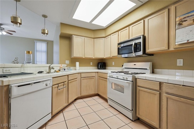 kitchen with light brown cabinetry, a sink, light tile patterned floors, a peninsula, and white appliances