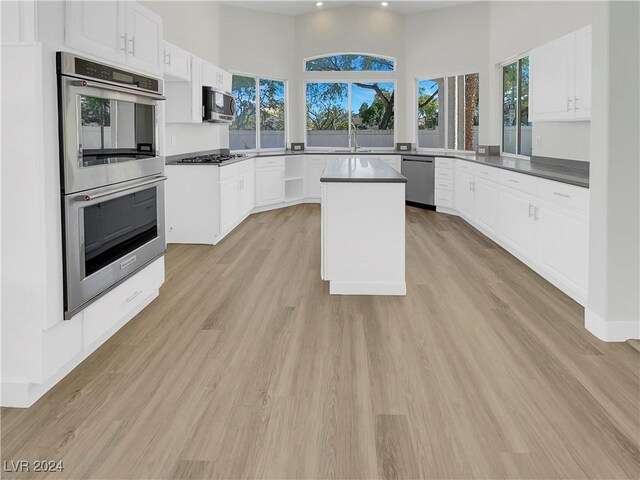 kitchen with a high ceiling, white cabinets, light wood-type flooring, a kitchen island, and stainless steel appliances