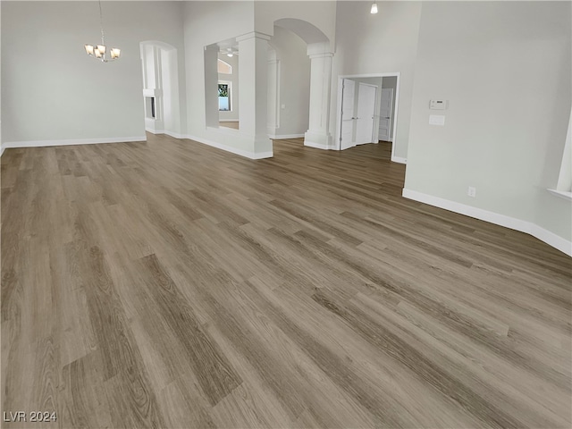 unfurnished living room featuring hardwood / wood-style floors, a chandelier, and decorative columns