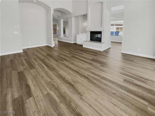 unfurnished living room featuring a multi sided fireplace, ornate columns, and hardwood / wood-style floors