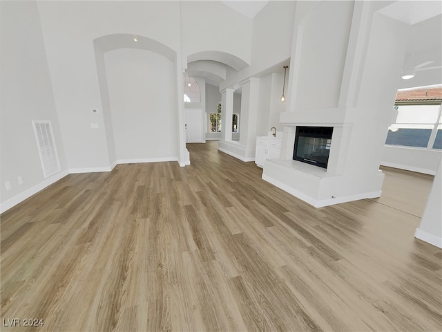 unfurnished living room with light hardwood / wood-style floors, a large fireplace, a healthy amount of sunlight, and a high ceiling