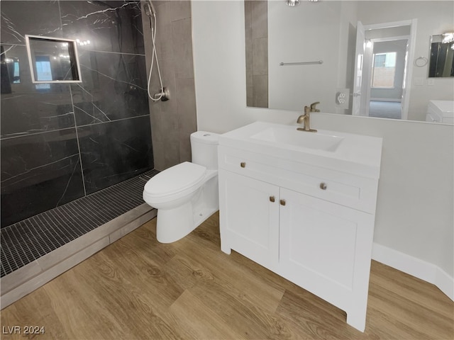 bathroom with hardwood / wood-style floors, vanity, toilet, and a tile shower