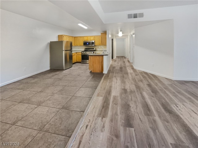 kitchen with light hardwood / wood-style flooring, stainless steel appliances, kitchen peninsula, sink, and light brown cabinets