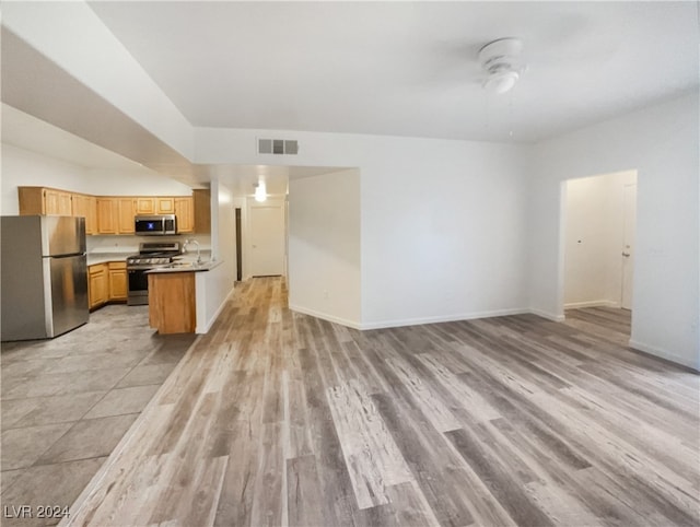 kitchen with light wood-type flooring, appliances with stainless steel finishes, light brown cabinets, kitchen peninsula, and ceiling fan