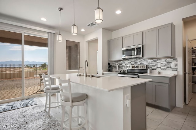 kitchen featuring an island with sink, hanging light fixtures, stainless steel appliances, a kitchen bar, and decorative backsplash