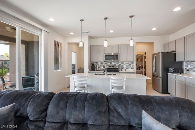 kitchen featuring gray cabinets, backsplash, an island with sink, hanging light fixtures, and appliances with stainless steel finishes