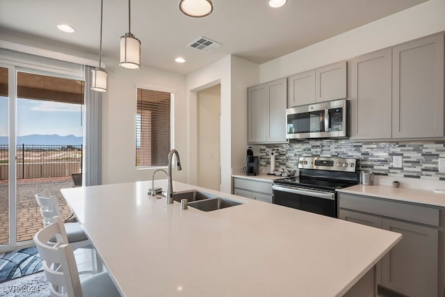 kitchen featuring pendant lighting, stainless steel appliances, a center island with sink, and sink