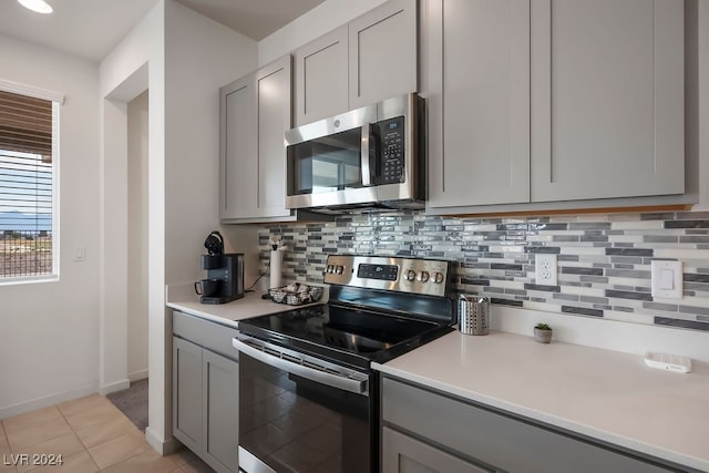 kitchen featuring gray cabinetry, appliances with stainless steel finishes, light tile patterned floors, and backsplash