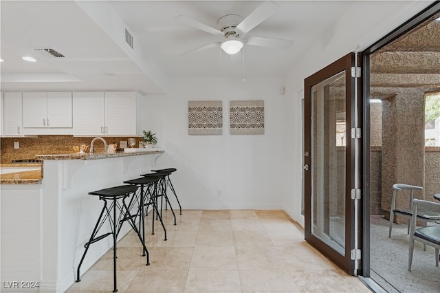 kitchen featuring light stone counters, white cabinetry, a kitchen breakfast bar, and kitchen peninsula