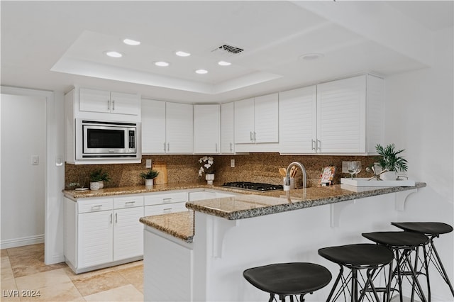 kitchen featuring light stone counters, appliances with stainless steel finishes, a raised ceiling, kitchen peninsula, and white cabinets