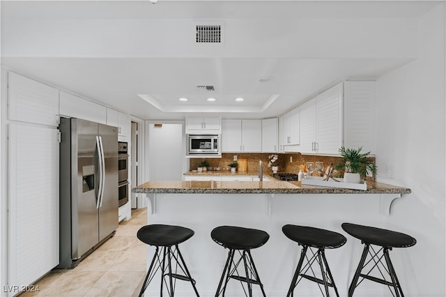 kitchen with white cabinetry, appliances with stainless steel finishes, kitchen peninsula, and a tray ceiling