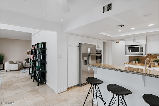 kitchen featuring stone counters, white cabinetry, backsplash, appliances with stainless steel finishes, and a kitchen breakfast bar