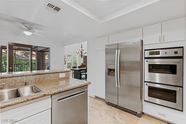 kitchen featuring light tile patterned flooring, ceiling fan with notable chandelier, white cabinetry, light stone counters, and stainless steel appliances