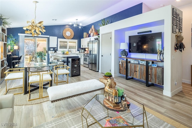 living room featuring an inviting chandelier, light hardwood / wood-style floors, wine cooler, and vaulted ceiling