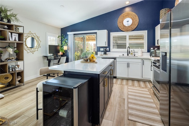 kitchen with light hardwood / wood-style flooring, stainless steel appliances, sink, white cabinetry, and lofted ceiling